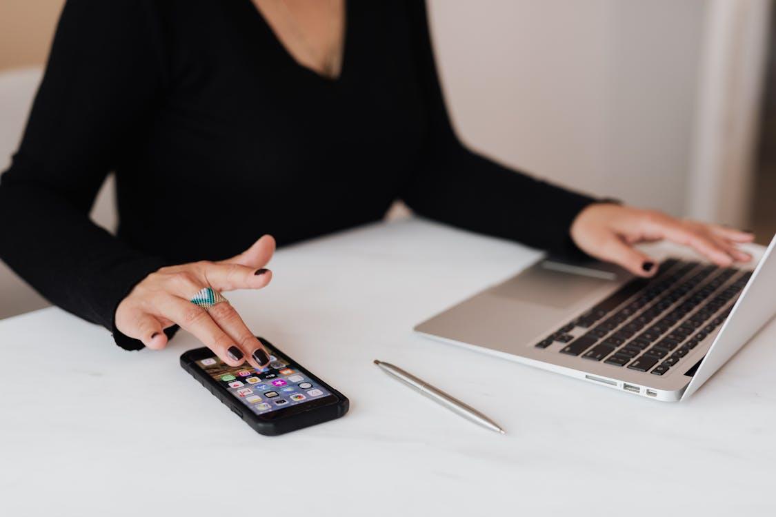 Free Crop woman using smartphone and laptop during work in office Stock Photo